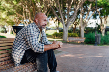 Fototapeta premium A man sits on a bench, holding his head in his hands. Distress, fear, emotions, problem