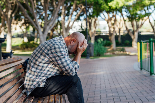 A man sits on a bench, holding his head in his hands. Distress, fear, emotions, problem