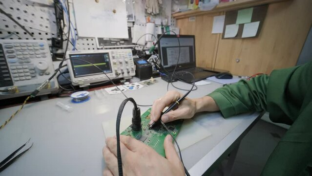 Electronic equipment repair shop. The Engineer Technician solders the printed circuit board of an electronic device under a microscope.