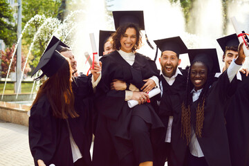 Smiling happy diverse graduates students having fun in a university graduate gown holding diploma...