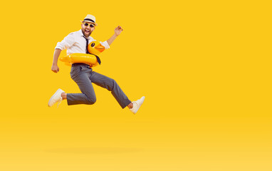 Funny happy man in office clothes, sunglasses and with duck rubber ring is going on summer holiday trip and having fun jumping on a yellow background with copy space. Vacation and travel concept.