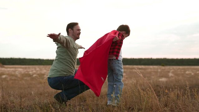 Father and son in red cape play superheroes soaring through air in imaginations