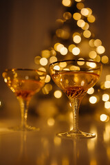 Two glasses of champagne are on the New Year's table. Christmas tree with garlands