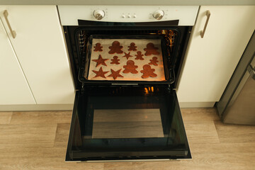 Cut out Christmas cookie dough shapes lie on a baking sheet in the oven