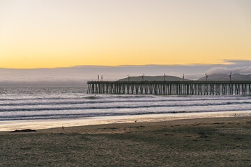 A mesmerizing sunset paints the sky with warm hues as the silhouette of a long pier extends gracefully on the horizon