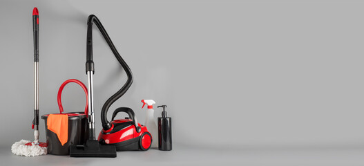 Cleaning concept mop and bucket, vacuum cleaner. Cleaning products and spin mop with red details on the floor in the grey background - obrazy, fototapety, plakaty