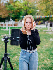 A teenage blogger girl shoots videos, records content. A blogger records a video on a mobile phone . A young girl is photographed in the park. An active lifestyle.