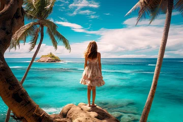 Foto op Canvas Girl in summer dress on a palm tree on a paradise beach looking at the sea © Александр Марченко