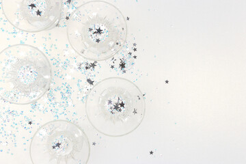Crystal glasses and stars confetti on a silver glittering background. Festive concept.