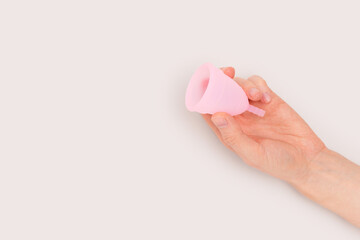 Female hand hold pink menstrual cup on a gray background. Minimal composition with copyspace. - obrazy, fototapety, plakaty