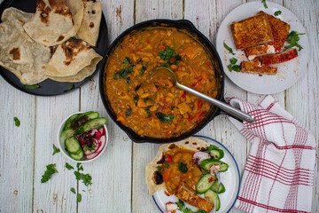 Mexican vegan spread consisting of refried beans stew, chili tofu and tortillas. White table, cast iron and ceramic dishes