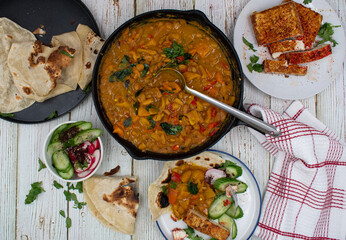 Mexican vegan spread consisting of refried beans stew, chili tofu and tortillas. White table, cast iron and ceramic dishes