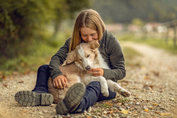 A young woman and her border collie puppy dog cuddling and interacting together in autumn outdoors, dog and owner concept - Powered by Adobe