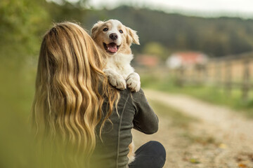 A young woman and her border collie puppy dog cuddling and interacting together in autumn outdoors, dog and owner concept
