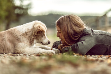 A young woman and her border collie puppy dog cuddling and interacting together in autumn outdoors,...