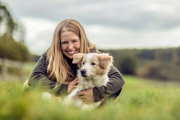 A young woman and her border collie puppy dog cuddling and interacting together in autumn outdoors,...