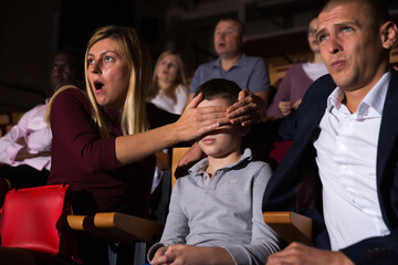 mother, father and their son sitting at scary perfomance in theatrical auditorium