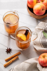 Homemade apple cider with apples and cinnamon in glasses on a light background with fresh fruits, spices and shadows. The concept of an autumn or winter healthy drink.