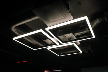 Modern office lighting. Thin lamps in office dark ceiling. LED white cold light over workplaces.