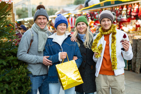 Cheerfull Family With Two Teenagers Posing With Christmas Gifts At Xmas Market