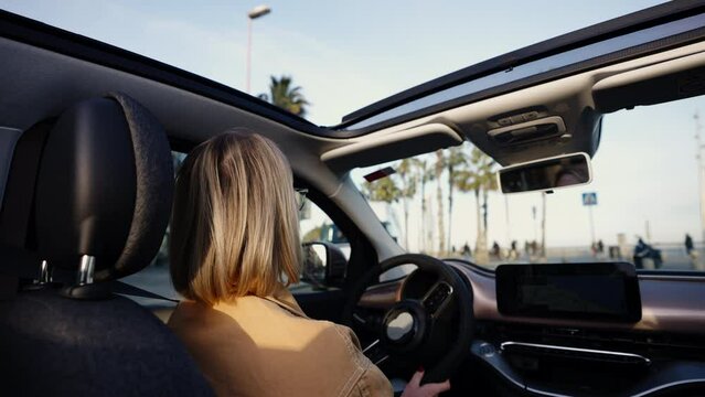 Profile view of focused blonde woman driving car with open sunroof, navigation on display, urban environment, concept of navigation and modern commute