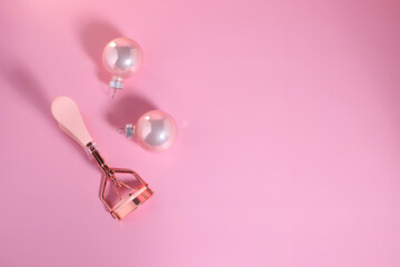 Eye lashes curler and Christmas decoration ball on pink background, beauty device