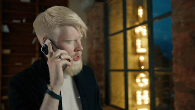 Close up of albino businessman calling on smartphone with night city lights on background. Male executive discussing project with colleague. Angry man arguing on mobile phone. Guy waving head no 4K