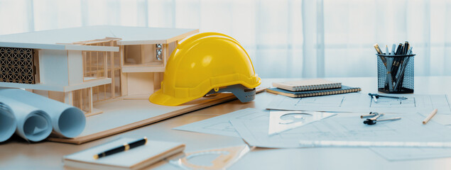 Yellow safety helmet was placed with architectural equipment, house model and blueprint scatter...