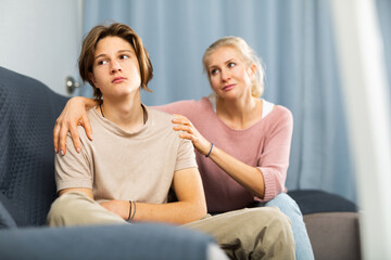 Obraz premium Upset teenager boy after quarrel with his mother in domestic interior, mother consoles son