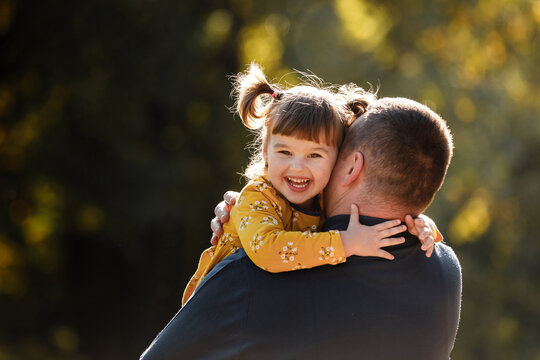Joyful dad hugs his little smiling daughter. Single daddy and child have fun, laugh and enjoy nature outdoors at autumn park. Concept of parental care and happy carefree childhood. Happy fathers day