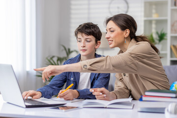 Mother and son studying together sitting at desk at home in living room, boy and woman tutor teaching at home, doing homework together