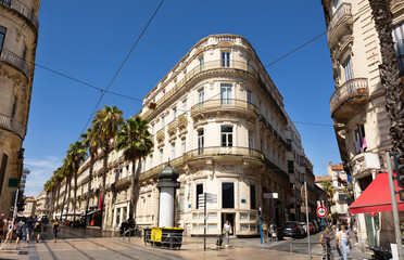 View of vibrant cobbled street with tram tracks, typical architecture and tall palm trees in French...