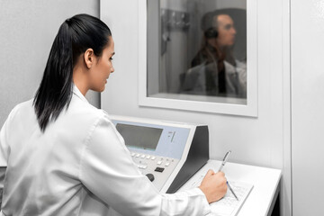 Audiologist woman doing the hearing exam to a mixed race man patient using an audiometer in a...