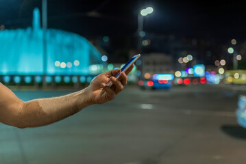 Male hand holding touch screen mobile phone on blurred night-lights