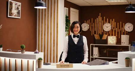 Happy professional asian hotel employee taking phone calls while working at reception counter. Joyful smiling receptionist taking travel accommodation booking requests standing at check in front desk