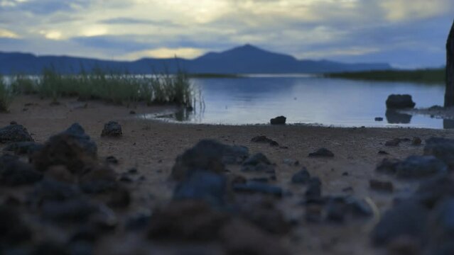 Shore of a calm lake with sand, grass and rocks