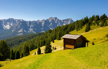 Obraz premium Tranquil peaceful landscape of green mountain valley bathed in summer sun with rustic wooden cabins in Dolomites ..