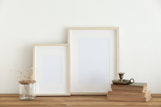 Horizontal wooden frame mockup on a vintage wooden table. Vintage candlestick on books, vase with white dry grass and flowers on white wall background. Scandinavian room interior design. selective