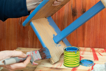 Mano con pincel y pintura azul, pintando un banco de madera.