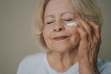 Close-up portrait of beautiful senior woman gently applying under eye face cream while closing her eyes. Product for beauty skincare - Powered by Adobe
