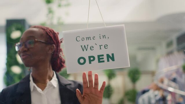 Worker finally reopening store after restocking elegant high end fashion boutique. Woman turning closed sign from clothing store door after adding stylish garments from new collection