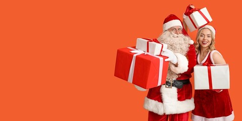 Santa Claus and young woman in Christmas costume holding gifts on orange background with space for...