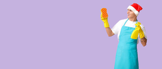 Male cleaner in Santa hat and with supplies on lilac background with space for text