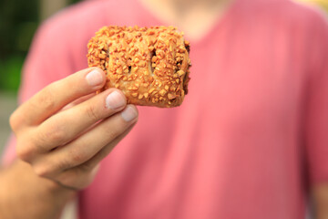 A guy's hand holds sweet pastry with jam, snack and fast food concept. Selective focus on hands with blurred background