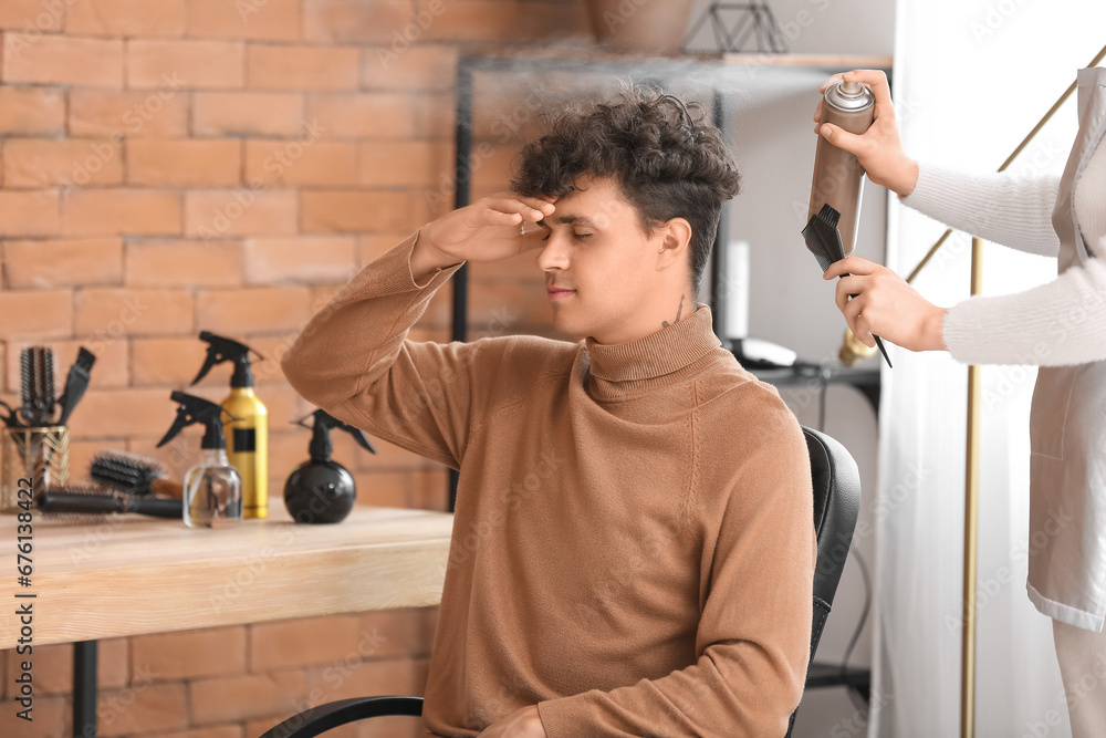 Canvas Prints Professional hairdresser applying hair spray on young man's curly hair in beauty salon