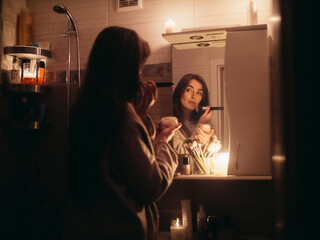 young woman doing make-up in a bathroom without electricity by candlelight