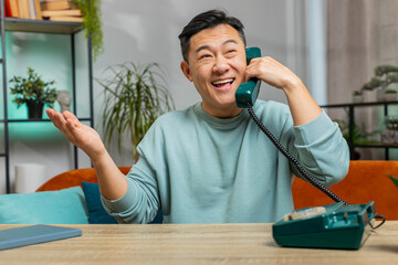 Portrait of Asian man making wired telephone conversation with friends sitting call on couch at...