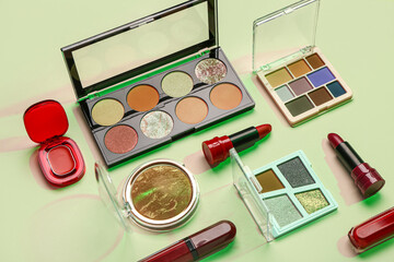 Beautiful palettes of eyeshadows and different decorative cosmetics on green background