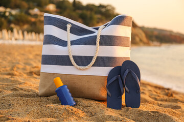 Stylish beach bag, flip-flops and sunscreen cream on sand