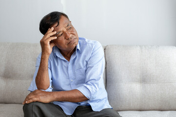 Asian retired elderly thinking and looking away sitting on the sofa alone at home, feeling sad or worried